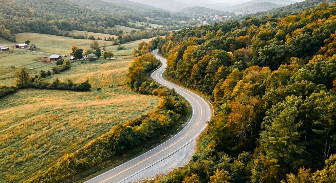 Aerial view of a winding road through New River Valley's forested Appalachian hills at golden hour.